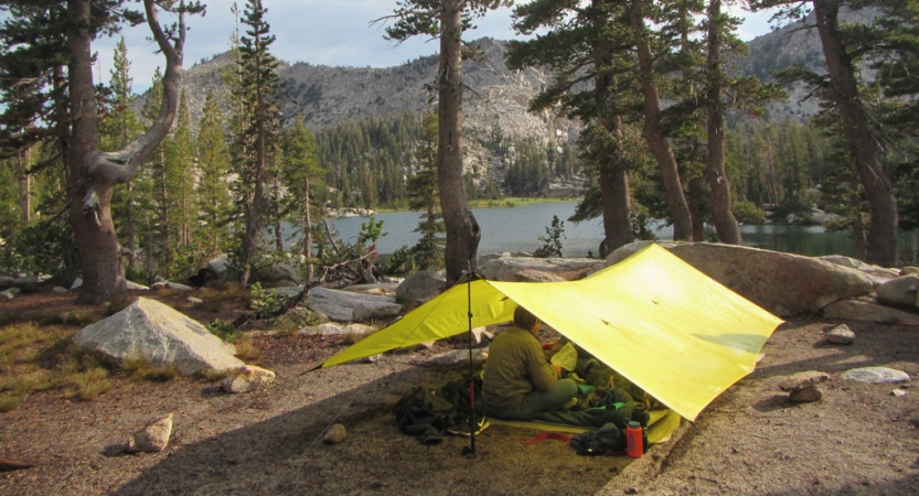 a person rests under a tarp shelter near a body of water on an outward bound course for bipoc